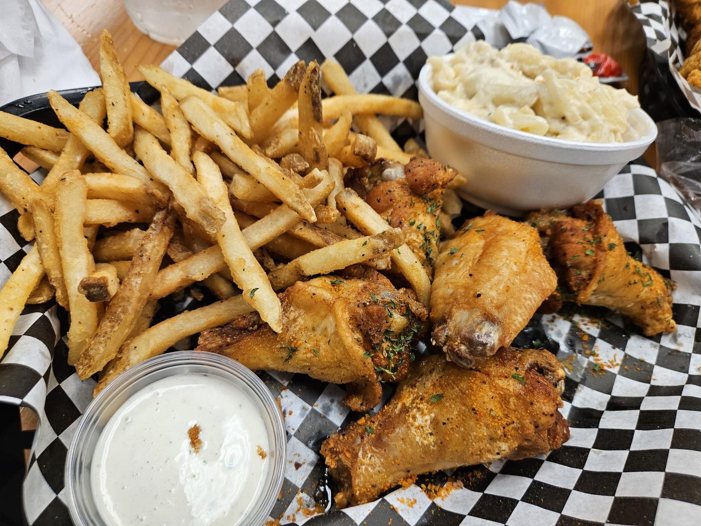 Seasoned wings and fries in a basket with ranch and mac and cheese