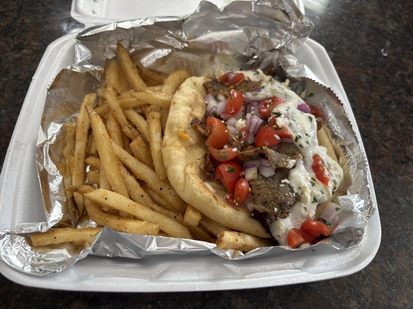 A gyro with lamb, tzatziki, tomato and red onion, served with fries